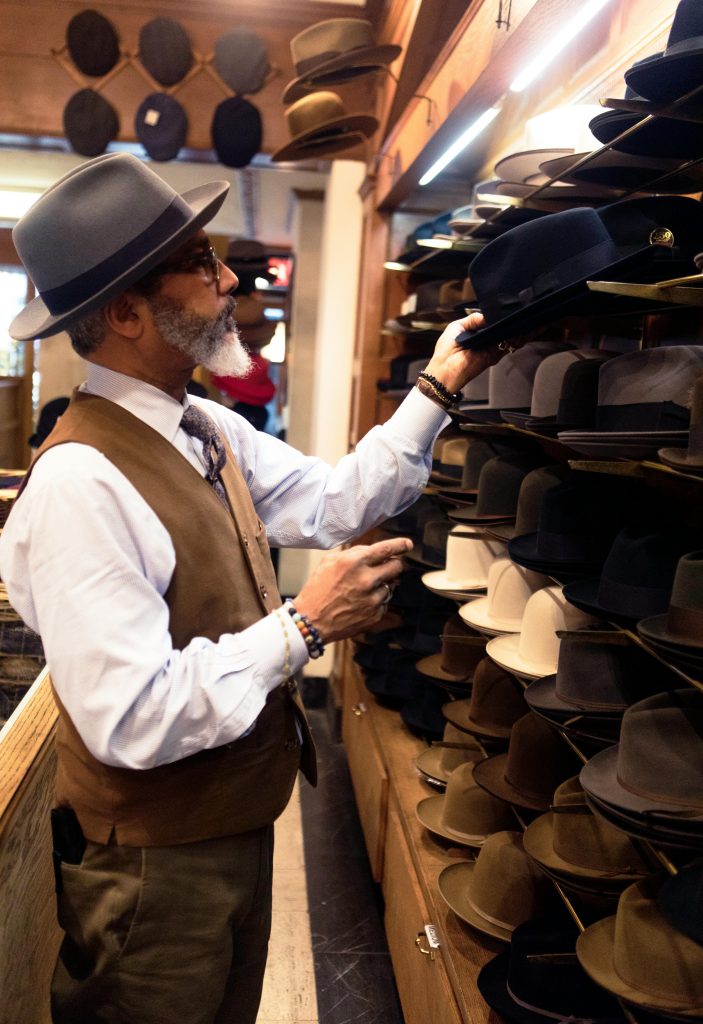 An adult man selects a hat from a variety displayed on shelves inside a stylish store.